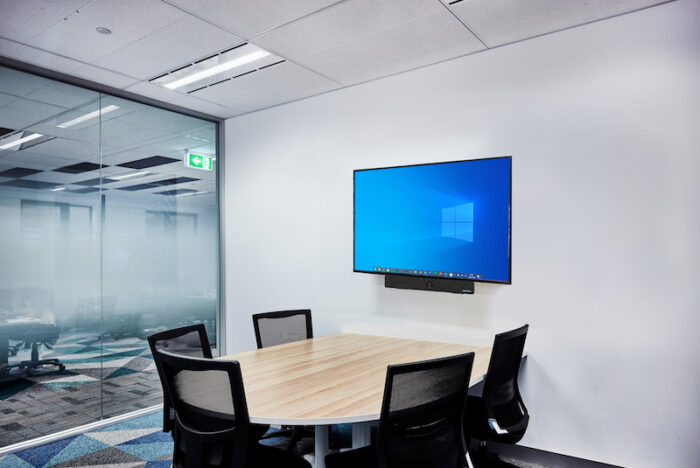 Interior photography of a small meeting room with wall mounted screens, sound proofing panels and timber meeting table and chairs